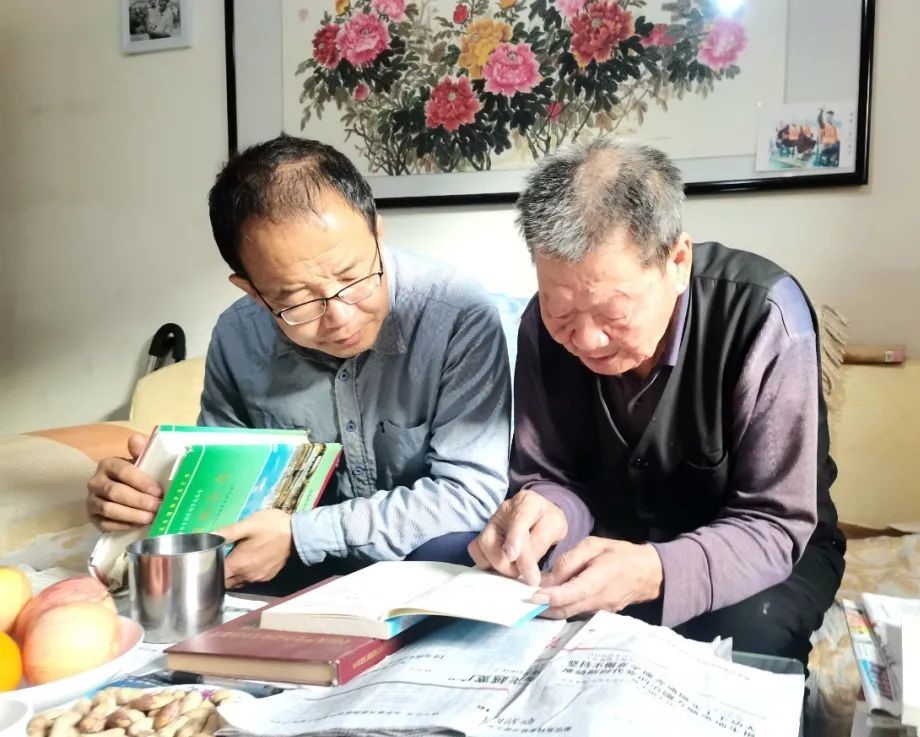 段进贤（右）翻看书籍，同记者讲述当年的故事。