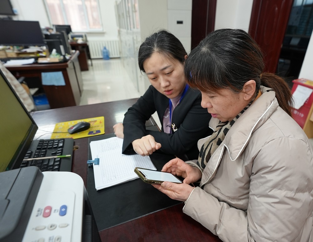1月10日，一五〇团社保分局工作人员焦丽玲（左）正在指导小商户老板马秀兰用手机微信小程序缴费。蒲晓霞 摄